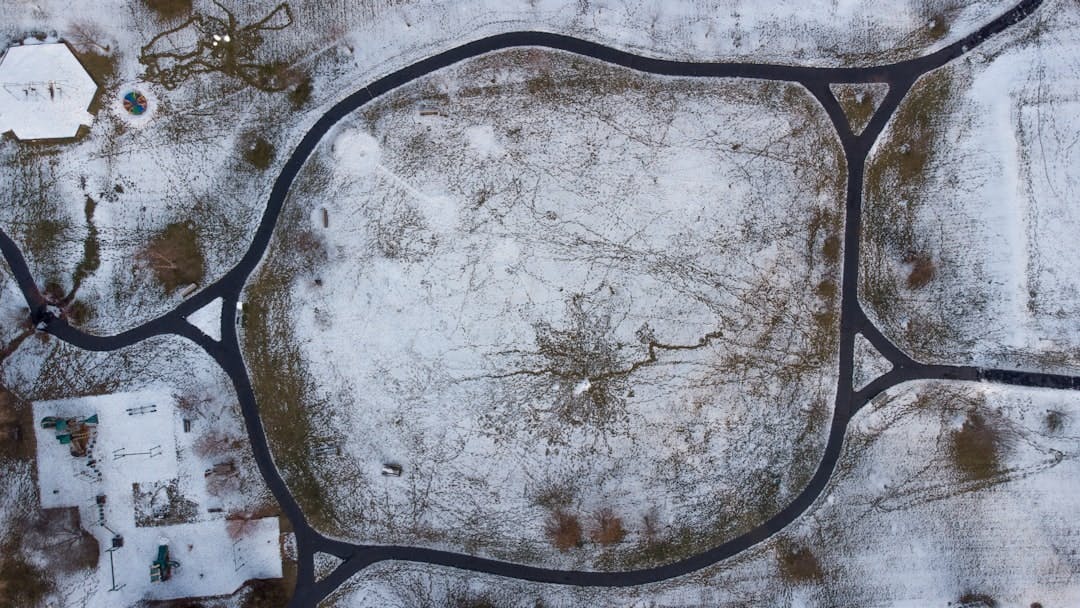 Looking down on a snowy park and playground from above with a long looping path creating a geometric pattern
